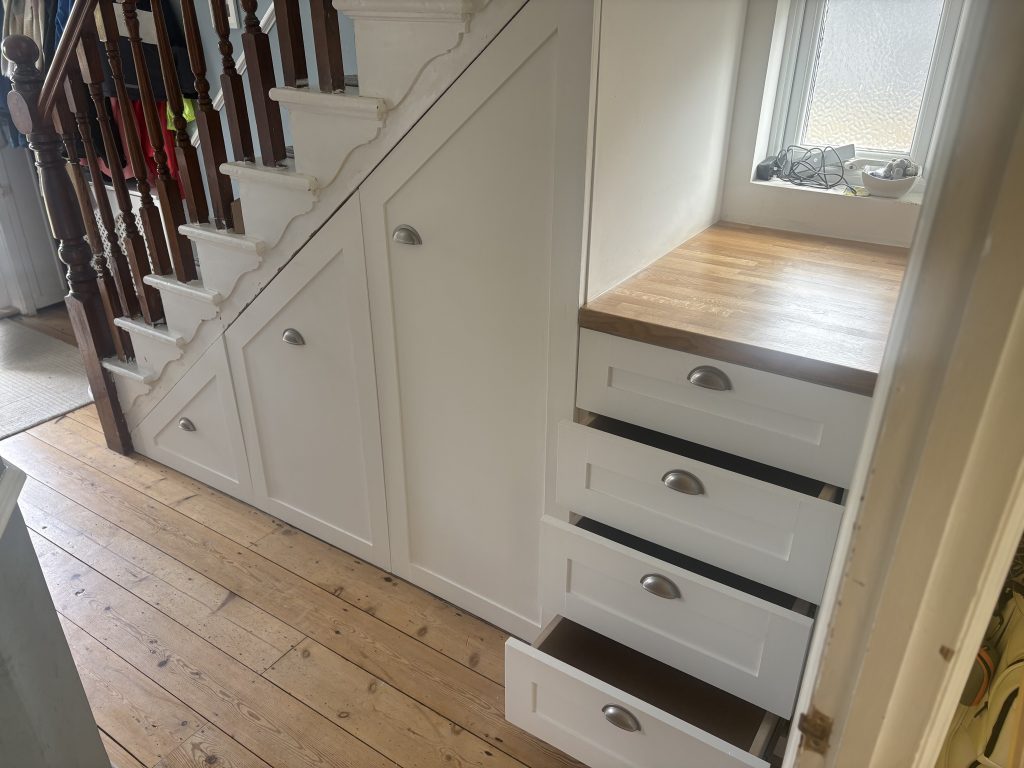 This image shows under stairs storage, with three large pull out units and four smaller pull out drawers. The drawers have a timber work survives.