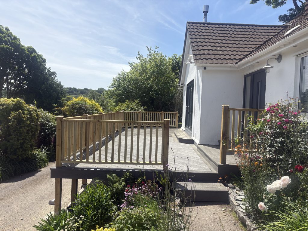 Image of a raised decking. The decking is made out of Millboard with a wooden handrail running around the outside edge.